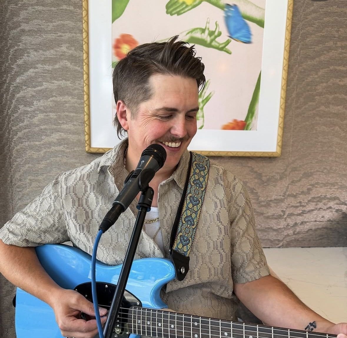 Jake Black smiling while playing a light blue electric guitar